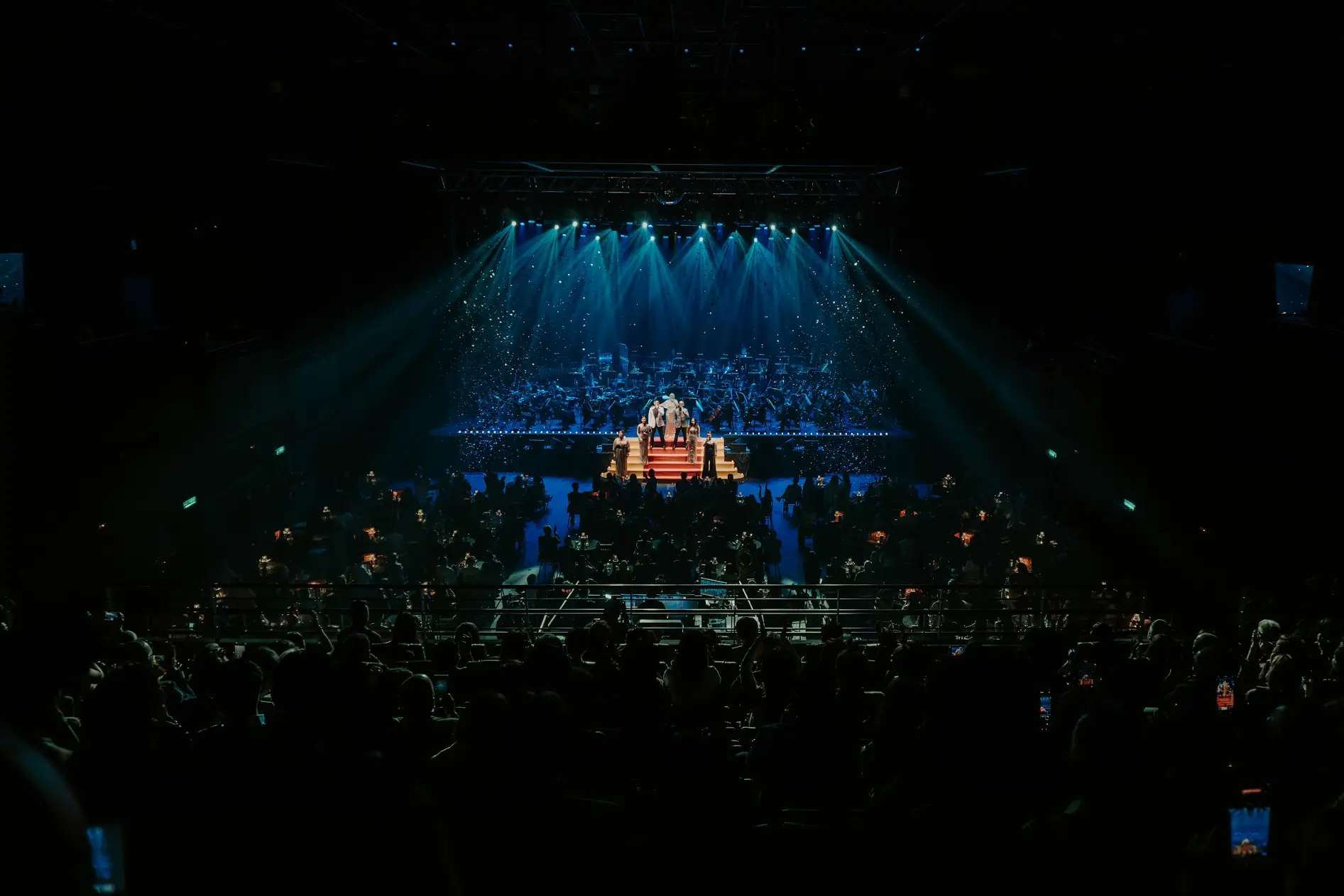 The auditorium end to end, the lit stage small and distant at the far end of it.