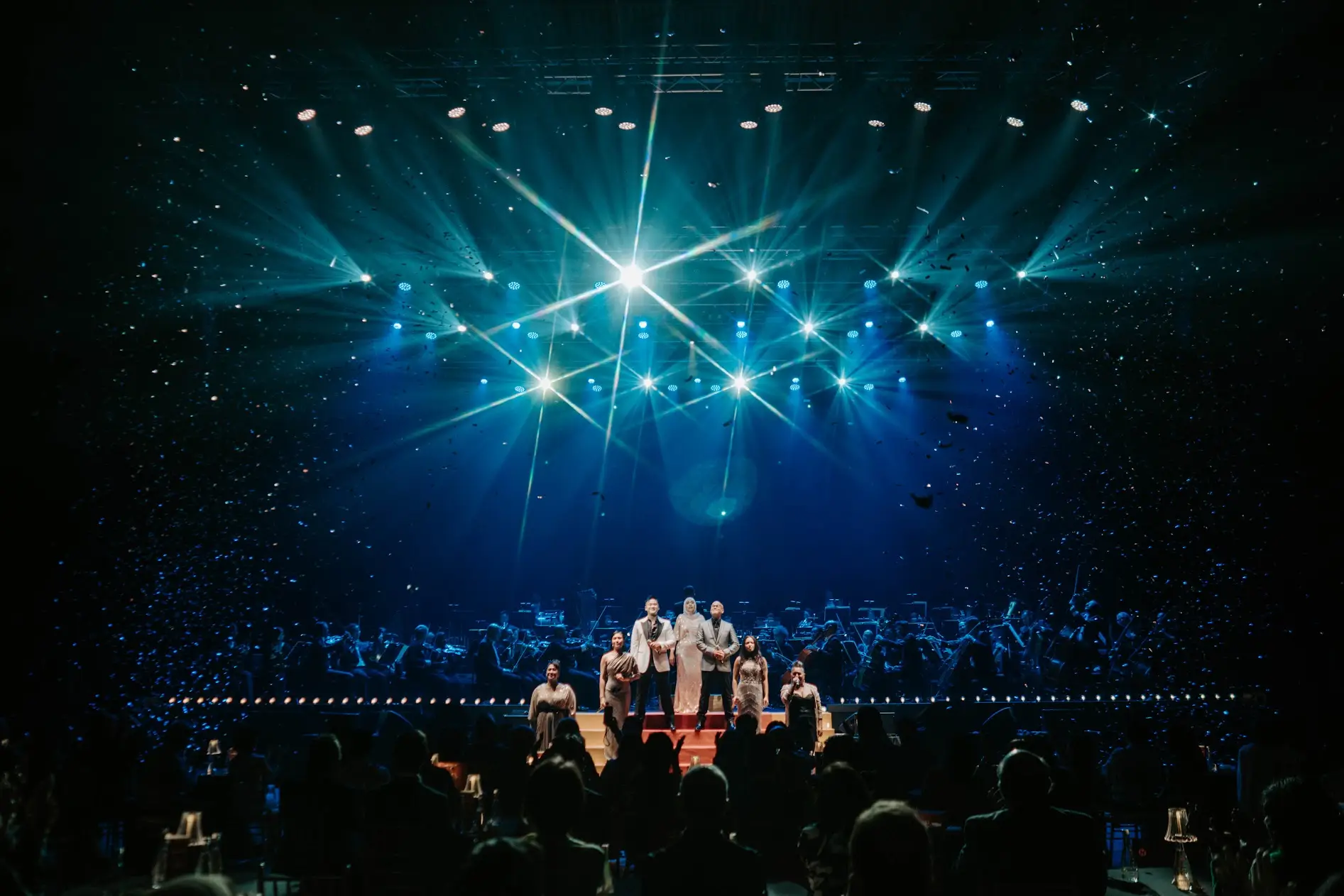 A starburst of white lights above the ensemble, the whole auditorium washed teal.