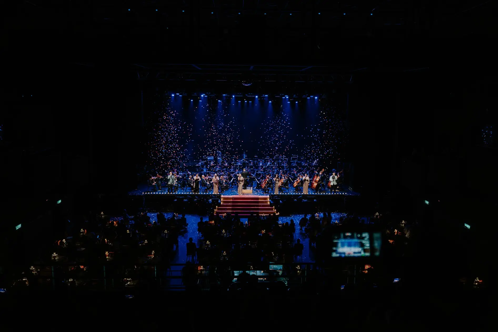 The full hall in deep blue, points of light falling like confetti over the stage.